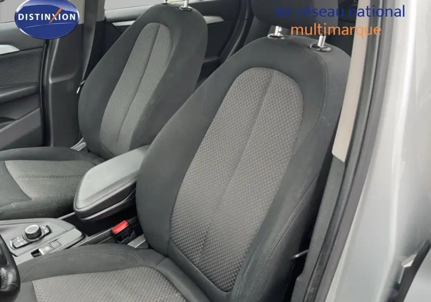 Vue intérieure rapprochée des sièges avant en tissu gris noir d’une BMW X1 18i gris argent 2018, porte ouverte côté droit.