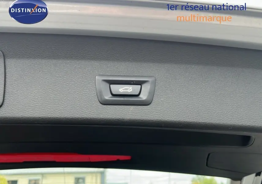 Détail du bouton d'ouverture électrique du coffre sur la partie intérieure du hayon d'un BMW X1 gris argent.