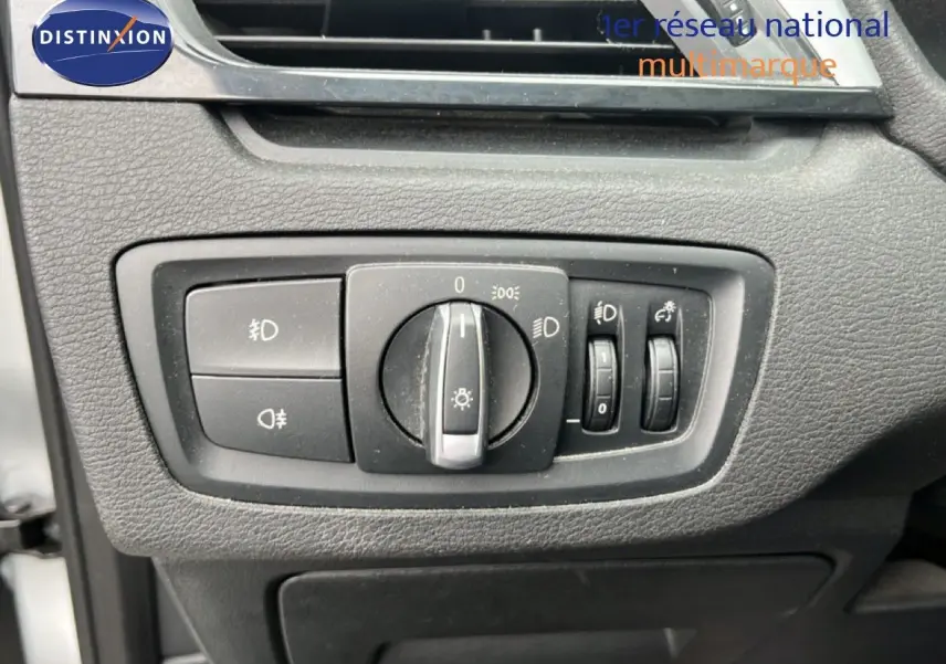 Gros plan sur les commandes d’éclairage intérieures du BMW X1 18i gris argent, avec boutons et molette de réglage.