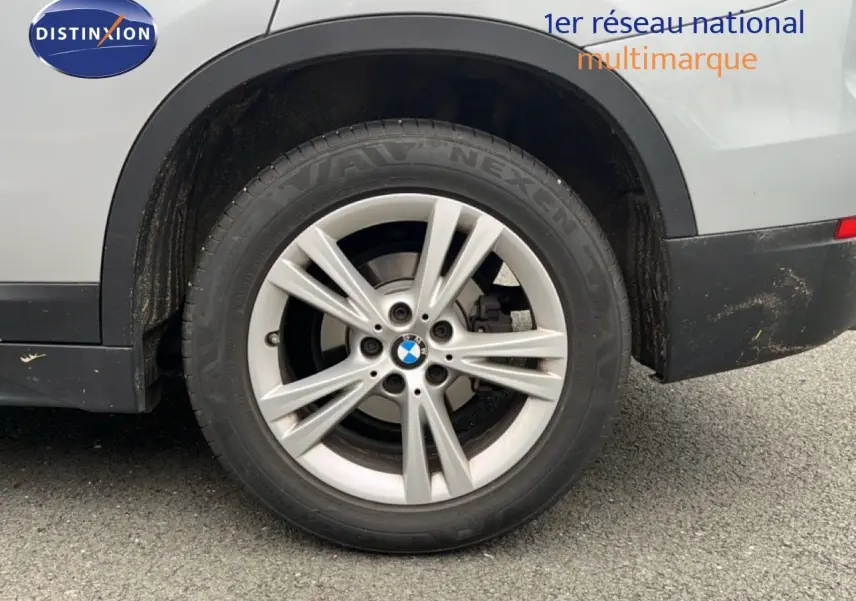 Gros plan sur la roue arrière droite d’un BMW X1 gris argent métallisé, avec jante alu 17 pouces et logo BMW visible.