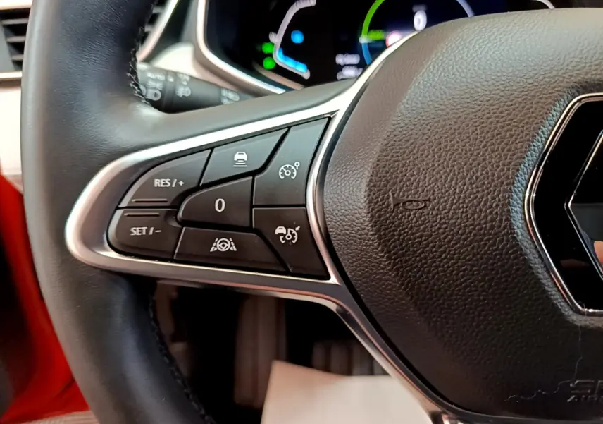 Gros plan sur le volant cuir noir de la Renault Clio Initiale Paris orange, avec commandes de régulateur de vitesse visibles à gauche.