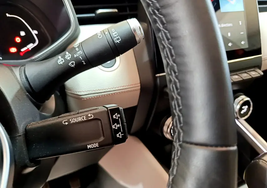 Vue rapprochée du volant noir et des commandes multimédia sur la gauche dans l'habitacle beige d'une Renault Clio orange.