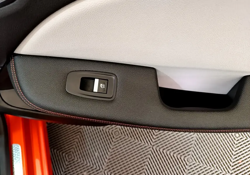 Gros plan sur la commande de lève-vitre côté gauche de la porte intérieure noire avec surpiqûres orange d'une Renault Clio orange.