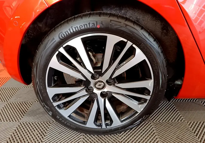 Gros plan sur la roue avant droite orange d'une Renault Clio Initiale Paris E-TECH 140 avec jante alliage bicolore.