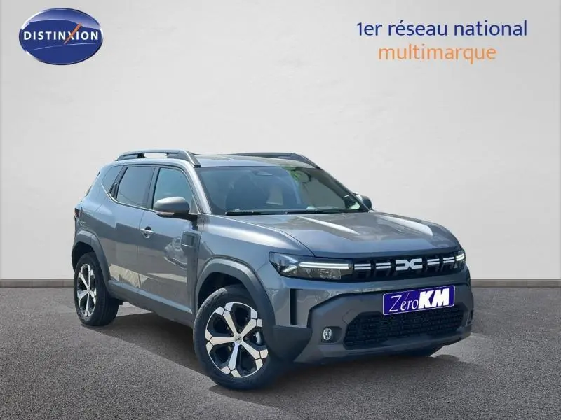 Vue 3/4 avant d'un Dacia Duster gris avec jantes alu et barres de toit sur fond neutre.
