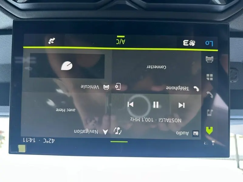 Écran tactile central du Dacia Duster blanc 2025 affichant les commandes audio et climatisation, vue de face rapprochée.