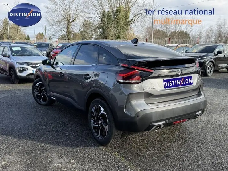 Citroën C4 gris 2024 vue 3/4 arrière droit, avec feux arrière distinctifs et jantes noires bicolores.