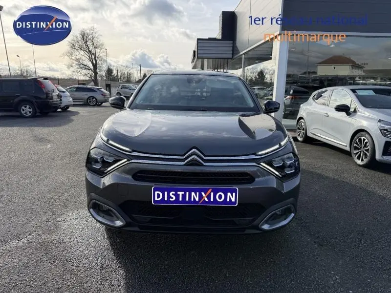 Vue de face d'une Citroën C4 gris 2024 avec calandre distinctive et phares LED, stationnée devant un showroom.