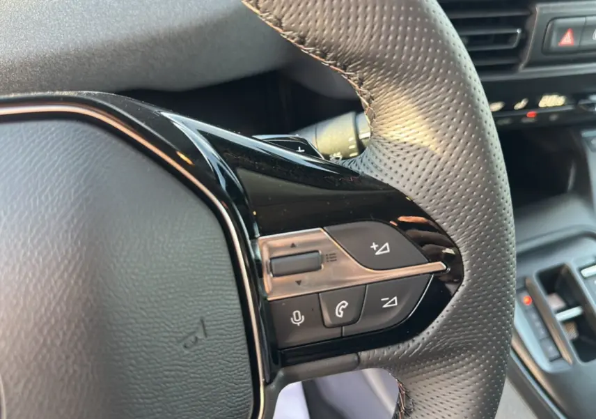Gros plan sur le volant cuir perforé du Peugeot Rifter GT Plus 2025 avec commandes multifonctions noires brillantes.
