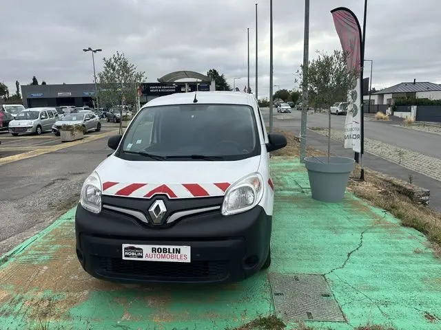 Vue avant d'un Renault Kangoo blanc 2020 avec bandes rouges diagonales sur le capot, garé sur un sol vert.