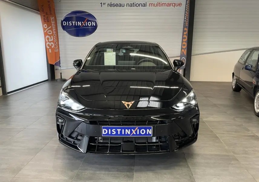 Vue de face d'une CUPRA Leon noire avec logo cuivré, phares allumés et calandre sportive en showroom.