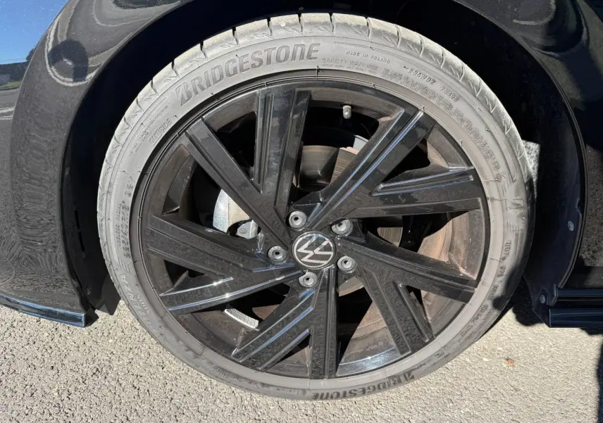 Gros plan sur la jante noire brillante de la Volkswagen Golf 2024, détail du pneu Bridgestone et logo VW central.