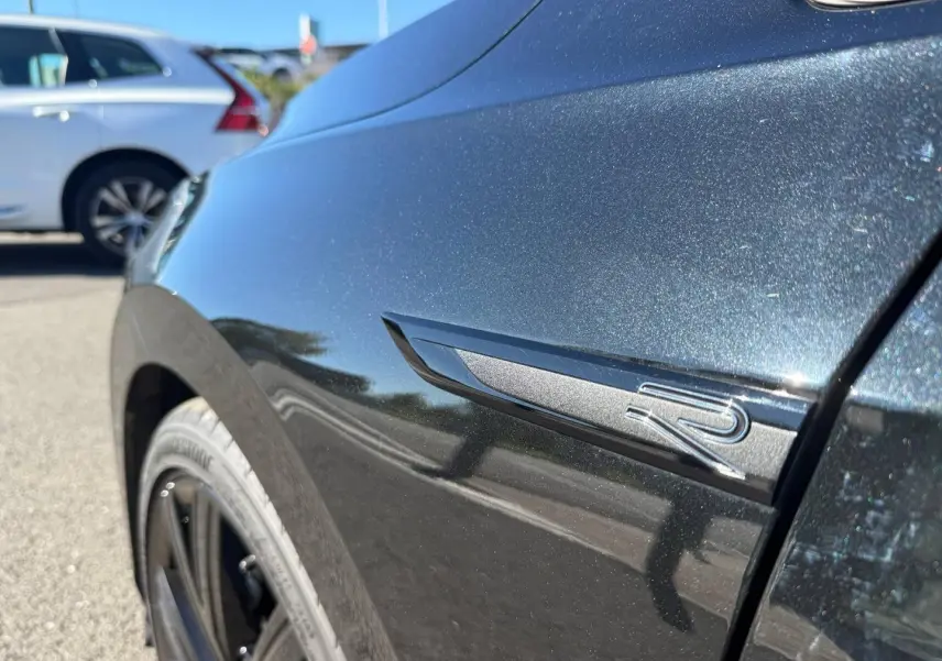 Gros plan sur l'aile avant droite noire métallisée Grenadilla avec logo R de la Volkswagen Golf 2024.