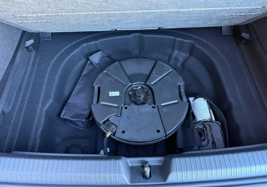 Vue plongeante sur le coffre ouvert d'une Volkswagen Golf noir, montrant la roue de secours et le rangement intérieur.