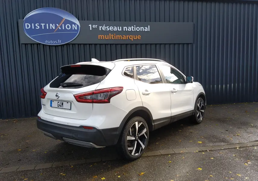 Nissan Qashqai blanc en 3/4 arrière droit, avec jantes alliage noires et toit ouvrant visible.