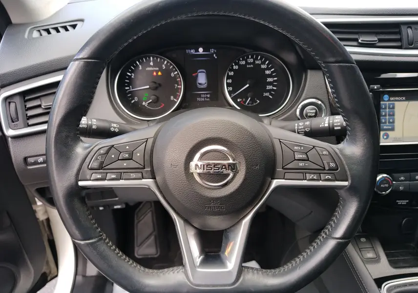 Vue rapprochée du volant en cuir noir d’un Nissan Qashqai blanc 2018, avec commandes intégrées et tableau de bord visible.