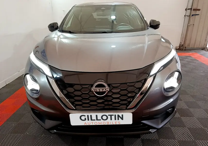 Vue frontale d'un Nissan Juke Hybrid 143 Business+ gris foncé avec phares allumés et calandre noire hexagonale.