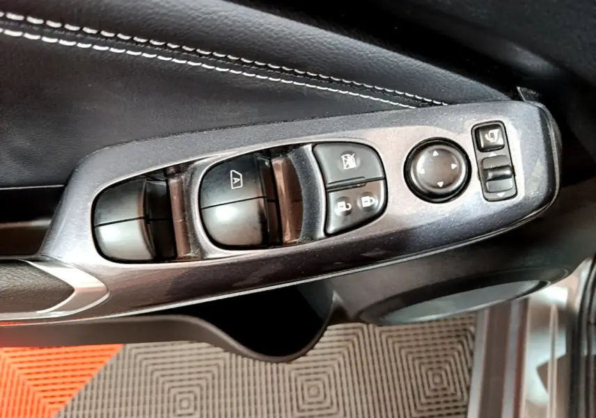 Gros plan sur les commandes de lève-vitres et rétroviseurs côté conducteur du Nissan Juke Hybrid gris foncé 2023.