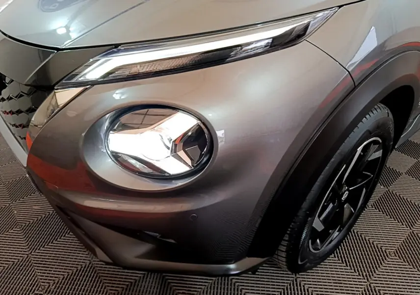 Gros plan sur le phare avant droit et la roue noire d'un Nissan Juke Hybrid gris foncé 2023.
