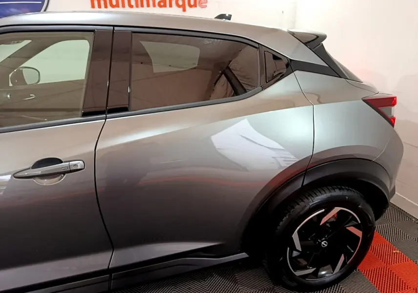 Vue latérale gauche du Nissan Juke Hybrid 143 Business+ gris foncé, soulignant la ligne de caisse et la jante noire à motifs géométriques.