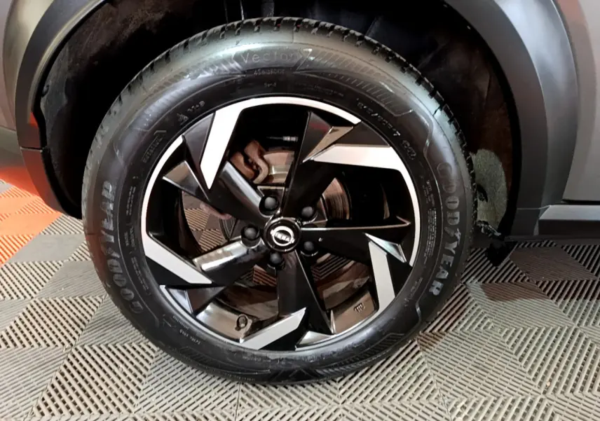 Gros plan sur la roue avant droite du Nissan Juke Hybrid 143 Business+ gris foncé avec jante noire et argentée design moderne.