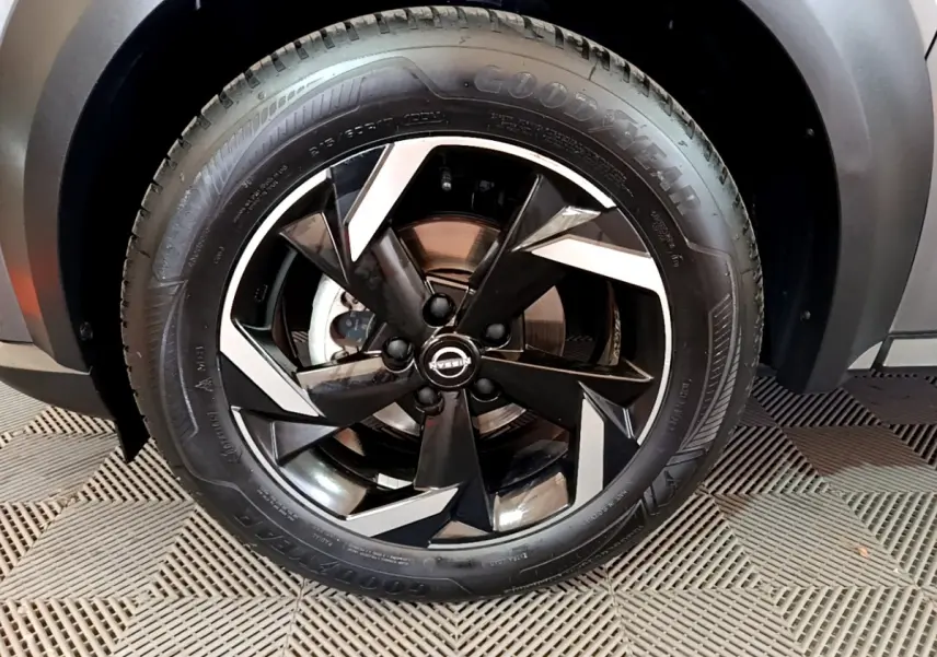 Gros plan sur la roue avant droite du Nissan Juke Hybrid 143 Business+ gris foncé avec jante noire et argentée design moderne.