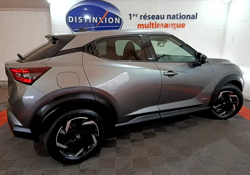 Profil droit du Nissan Juke Hybrid 143 Business+ gris foncé avec jantes noires et toit noir en intérieur showroom.