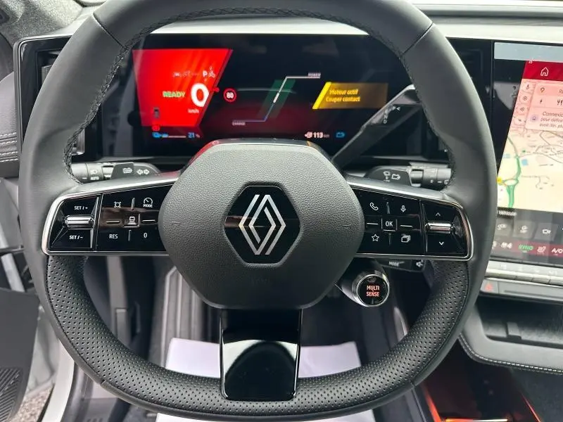 Vue rapprochée du volant multifonction noir avec logo Renault et tableau de bord numérique du Scenic E-Tech 2025.