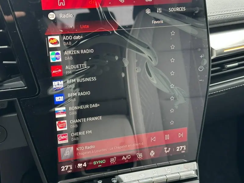 Écran tactile central affichant les stations radio dans l'habitacle d'une Renault Scénic rouge 2025 vue de face.