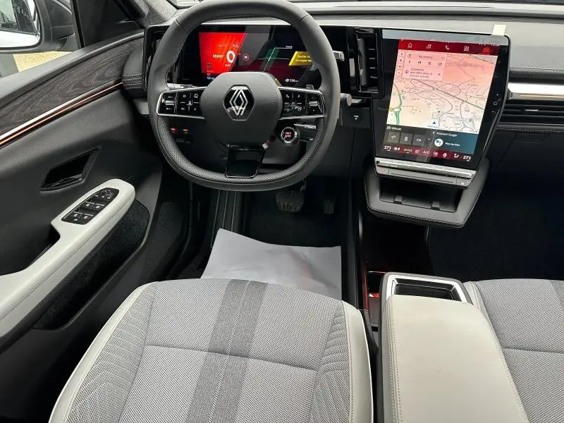 Vue intérieure avant du Renault Scénic E-Tech rouge, tableau de bord moderne avec écran tactile vertical et volant multifonction noir.