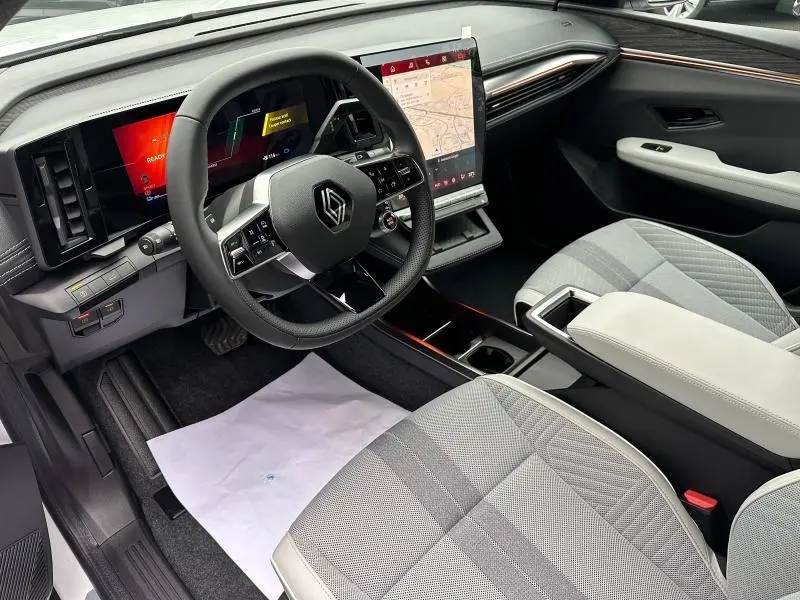 Vue intérieure côté conducteur du tableau de bord et volant noir avec écran tactile vertical et sièges gris clair du Renault Scenic E-Tech 2025.