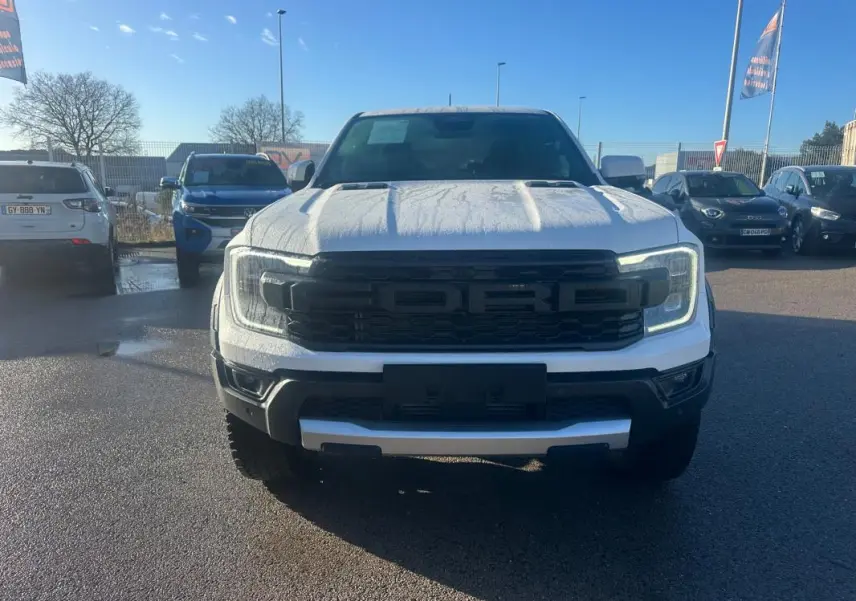 Vue avant d'un Ford Ranger Raptor blanc 2025 avec calandre noire marquée FORD et feux LED allumés.