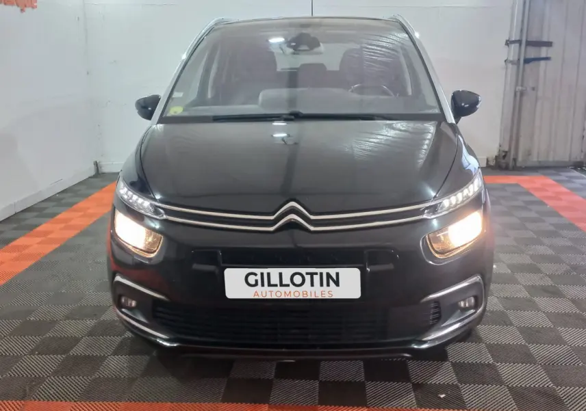 Vue frontale d'un Citroën Grand C4 Spacetourer noir avec phares allumés dans un garage.