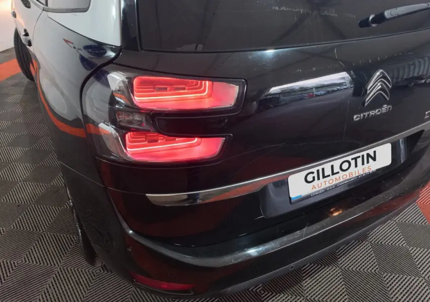 Vue arrière côté gauche d'un Citroën Grand C4 Spacetourer noir avec feux arrière allumés et logo visible.