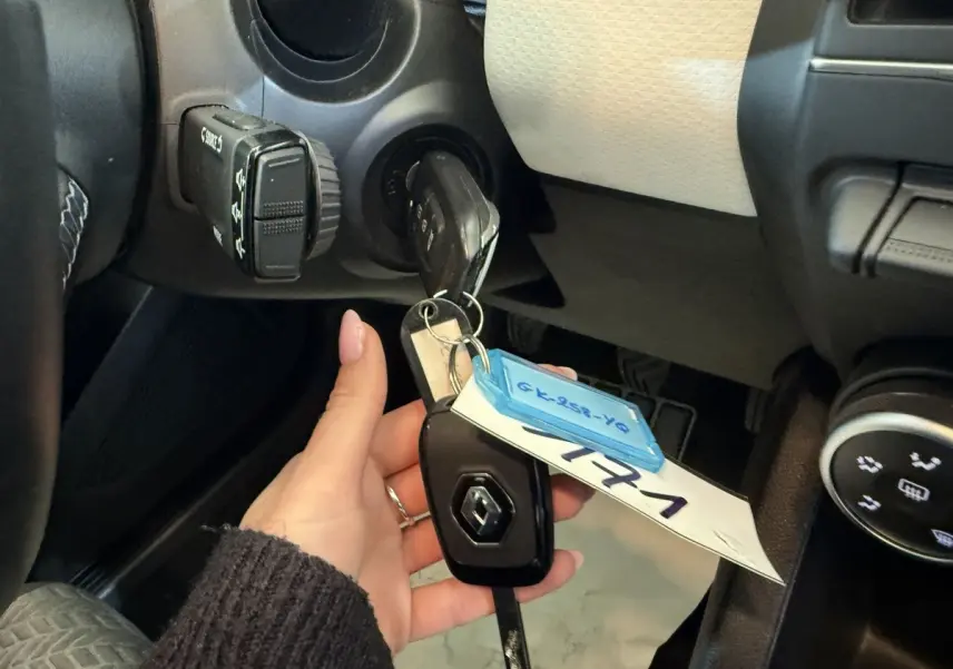 Main tenant la clé Renault insérée dans le contacteur, vue intérieure côté conducteur du tableau de bord noir et beige.