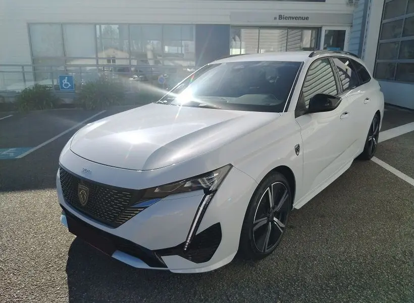 Peugeot 308 SW Hybrid 145 GT blanc Okenite vue 3/4 avant droit, avec calandre noire et jantes alliage noires.
