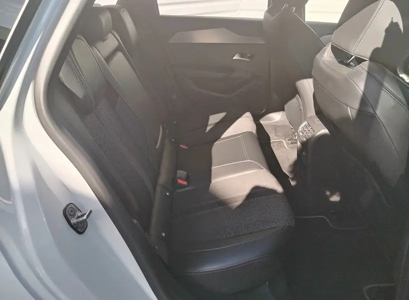 Vue intérieure arrière côté gauche du Peugeot 308 SW Hybrid 145 GT blanc Okenite, sièges en tissu noir avec surpiqûres.
