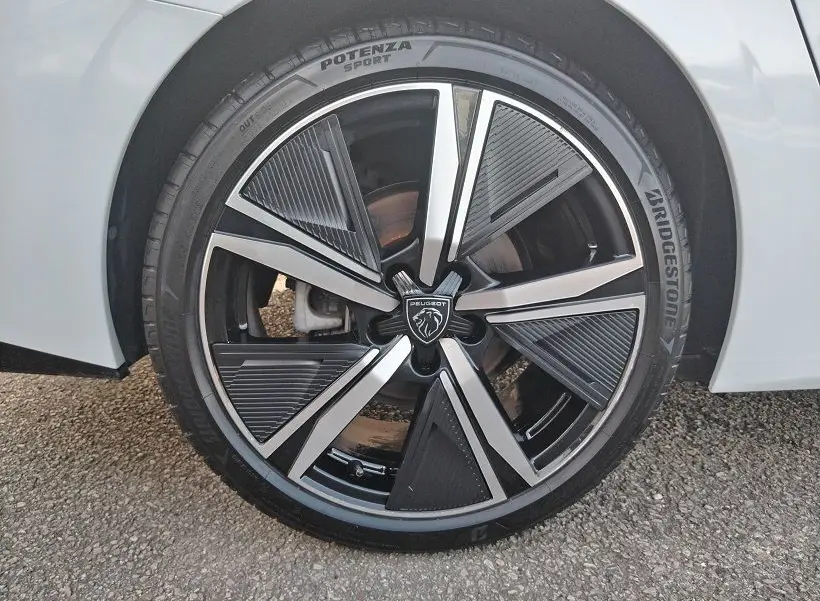 Gros plan sur la roue avant droite d’une Peugeot 308 SW Hybrid 145 GT blanche, avec jante noire et argentée au design moderne.