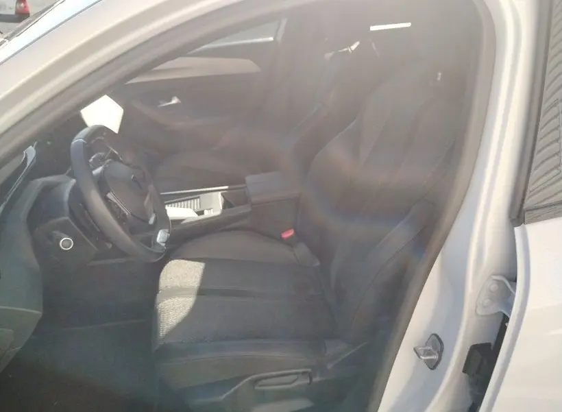 Vue intérieure côté conducteur du Peugeot 308 SW Hybrid 145 GT blanc Okenite, montrant le siège et le volant.
