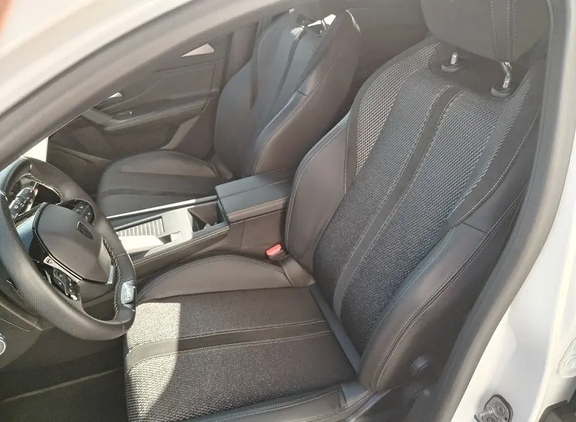 Vue intérieure côté conducteur de la Peugeot 308 SW Hybrid 145 GT, sièges noirs en tissu et cuir, volant multifonction.