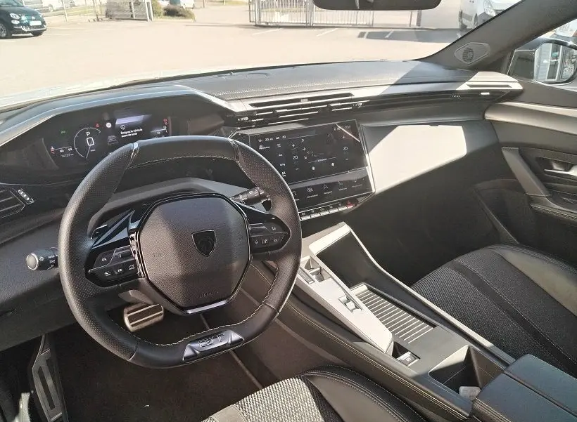 Vue intérieure côté conducteur du Peugeot 308 SW Hybrid 145 GT 2025, volant multifonction et tableau de bord digital.