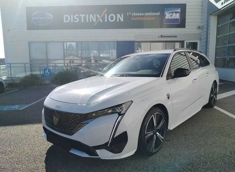 Peugeot 308 SW Hybrid 145 GT blanc Okenite vue 3/4 avant droit avec calandre noire et jantes alliage.