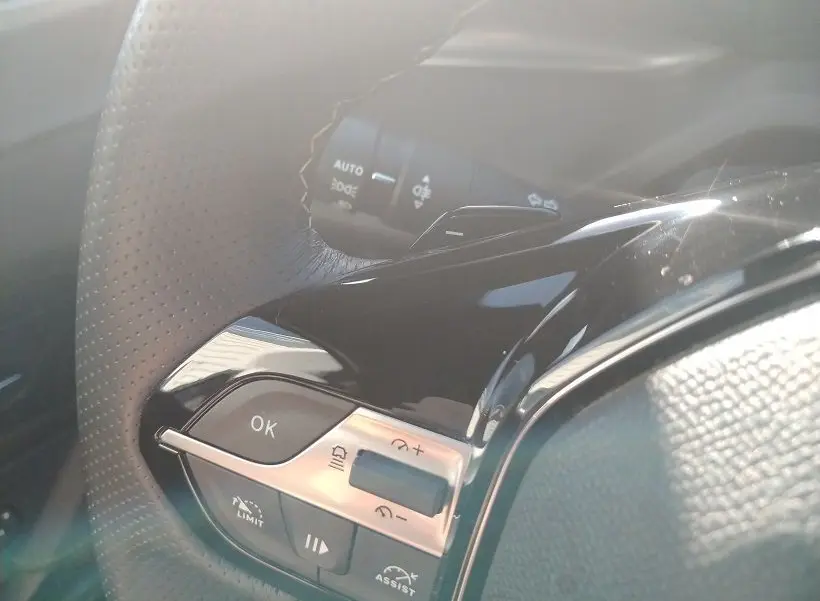 Gros plan sur les commandes au volant en cuir perforé du Peugeot 308 SW Hybrid 145 GT, finition noire brillante.