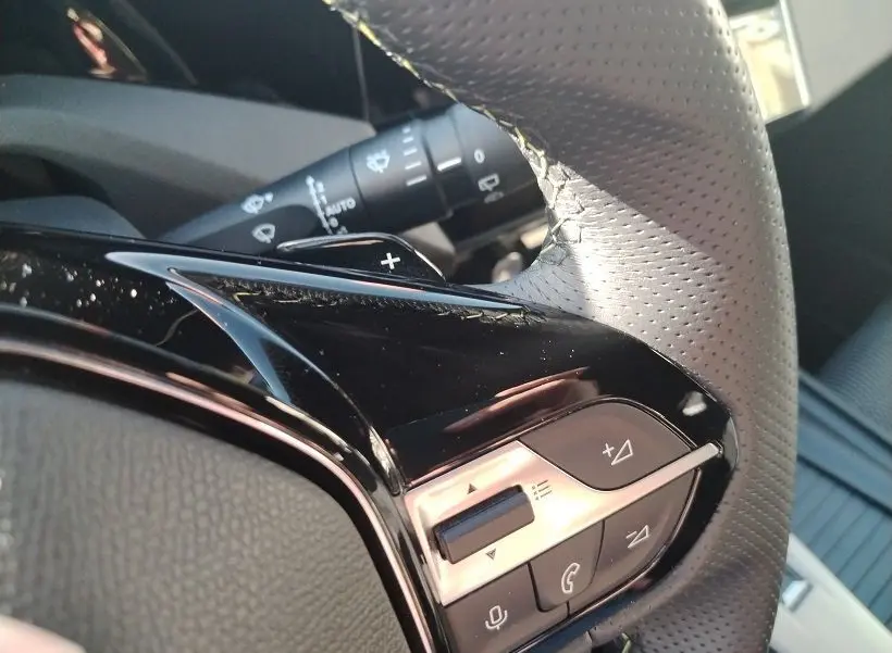 Gros plan sur les commandes au volant en cuir perforé noir et gris du Peugeot 308 SW Hybrid 145 GT, avec touches de réglage audio.