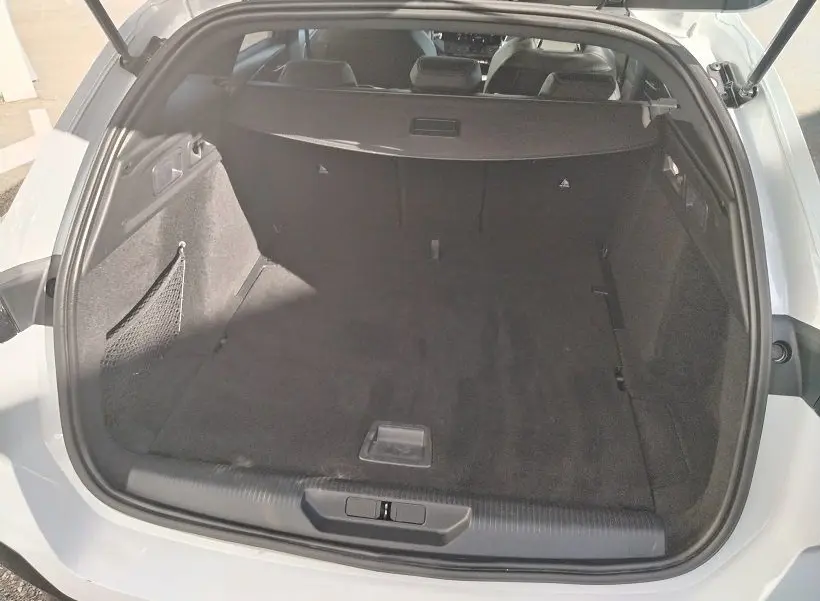 Coffre ouvert vu de l'arrière d'une Peugeot 308 SW Hybrid 145 blanc Okenite, espace de chargement spacieux et tapis noir.