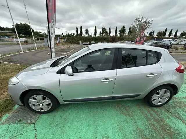 Vue de profil côté gauche d'une Renault Mégane 3 grise garée sur un sol vert, avec ses lignes épurées bien visibles.