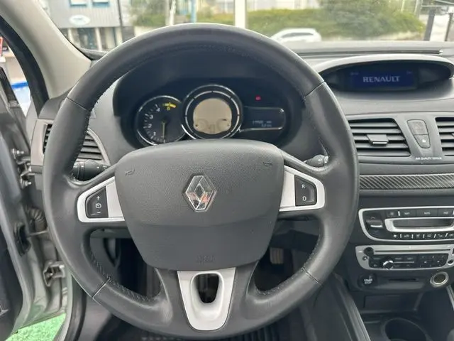 Vue intérieure centrée sur le volant noir de la Renault Mégane 3 gris, avec tableau de bord et console centrale visibles.