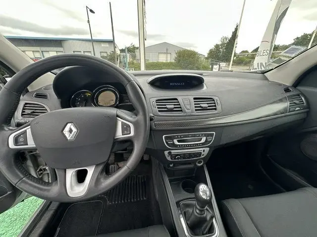 Vue intérieure du tableau de bord et volant de la Renault Megane 3 gris, avec levier de vitesse manuel et écran central Renault.