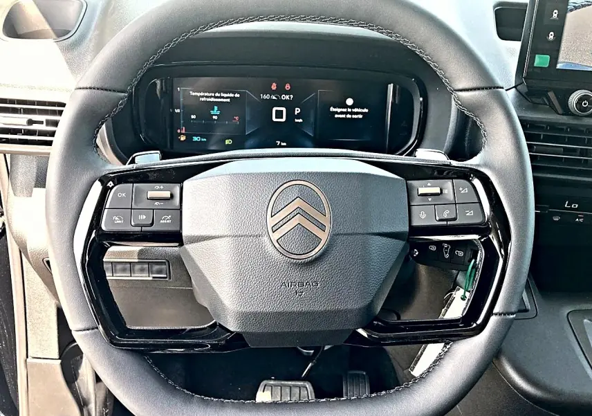 Vue rapprochée du volant cuir noir multifonction du Citroën Berlingo 2026 avec tableau de bord numérique en arrière-plan.
