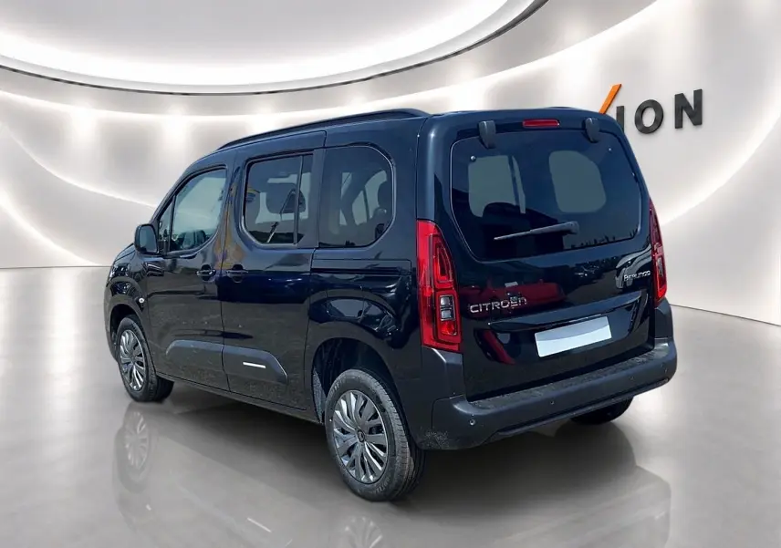 Vue 3/4 arrière droite d’un Citroën Berlingo noir avec barres de toit et vitres arrière teintées dans un showroom.
